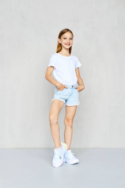 Young sportive girl in white t-shirt and jeans shorts posing in studio - Fotó, kép