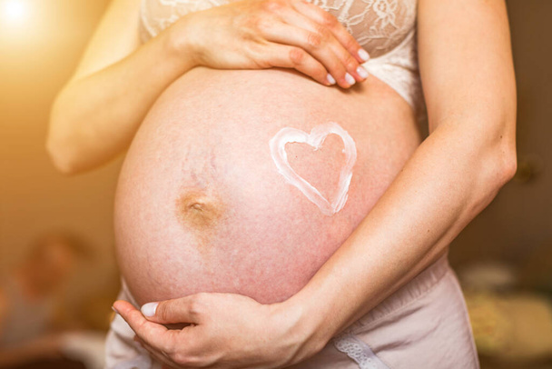 Közelkép egy terhes nő hasáról, szívet rajzolva a köldöke köré. Magas resulotiós kép. - Fotó, kép