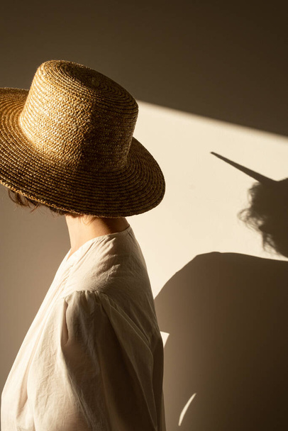 Young pretty woman in straw hat and white dress / sundress against the wall. Sunlight shadow on the wall. Minimal fashion design concept. - Foto, Imagem