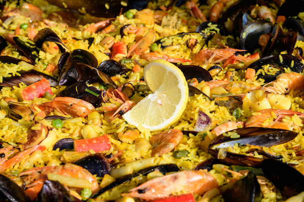 Close up of large portion of traditional Spanish paella dish freshly being cooked with seafood and rice in a frying pan at a street food festival, ready to eat seafood, side view, selective focus - Photo, Image