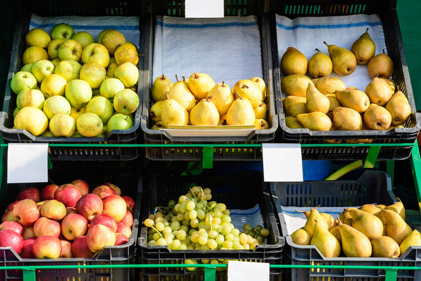 Fruits biologiques mûrs frais exposés à la vente dans un marché de rue à Bucarest, Roumanie, pommes vertes et lues, poires jaunes et raisins dans des boîtes en plastique avec des étiquettes blanches - Photo, image