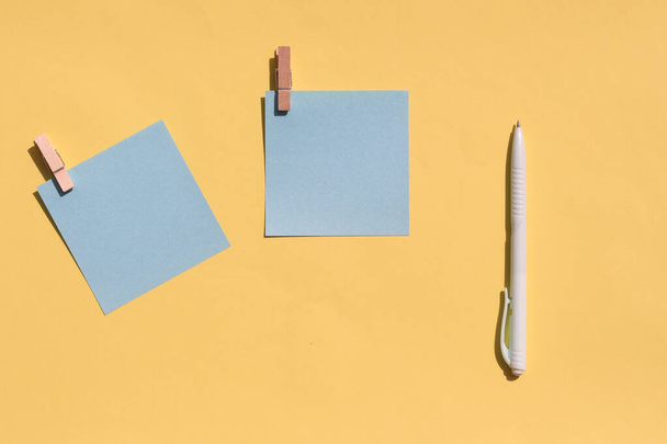 zwei blaue Blätter zum Schreiben und ein Stift auf gelbem Hintergrund. Ansicht von oben, Kopierraum. - Foto, Bild