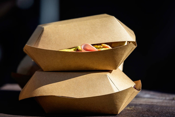 Zwei nehmen braune Pappkartons mit, die auf einem Holztisch auf einem Street-Food-Markt ausliegen, fertig zum Verkauf und essen gesunde Lebensmittel - Foto, Bild