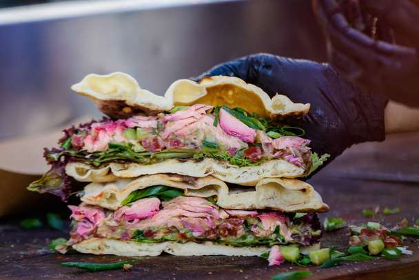 Coupe d'un sandwich ou d'un hamburger frais et sain coupé en deux côtés, préparé avec du guacamole de saumon et de la salade verte sur une table en bois marron dans un marché alimentaire de rue, vue de côté avec mise au point douce  - Photo, image
