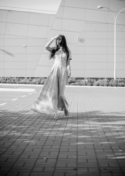 Όμορφο νεαρό κοκαλιάρικο κορίτσι περπατά γύρω από την πόλη σε ένα μακρύ φόρεμα σε ένα κλουβί και απολαμβάνει την ημέρα - Φωτογραφία, εικόνα