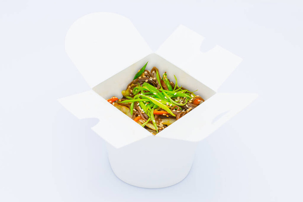 Izolált ázsiai Soba Buckwheat tészta zöldségekkel, szójaszósszal és újhagymás mogyoróhagymával fehér kartondobozban. Élelmiszer szállítási háttér kép. kész enni vegán fűszeres étel - Fotó, kép