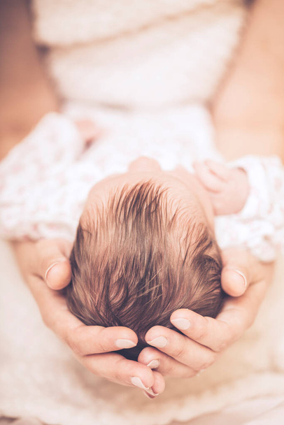 Rakastava äiti hoitaa vastasyntynyttä vauvaansa kotona. lähikuva onnellisesta äidistä pitelemässä nukkuvaa vauvaa kädestä. Äiti halaus hänen pieni tyttö. - Valokuva, kuva