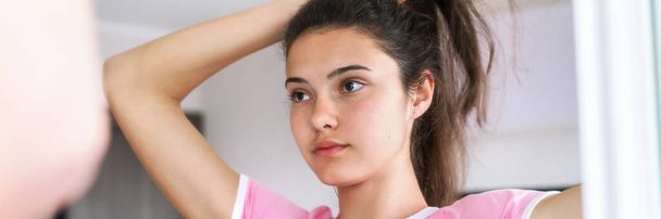 teenage brunette makes hairstyle reflecting in mirror - Fotó, kép