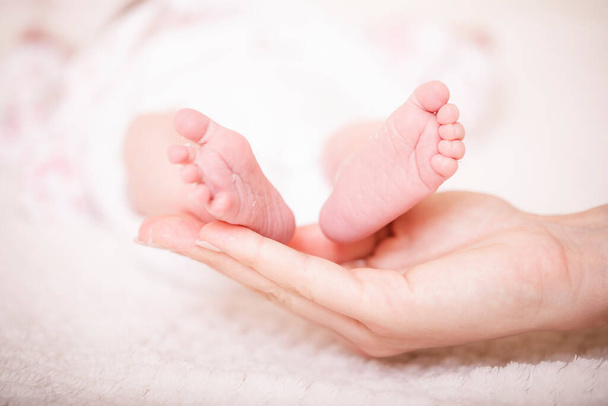 母親の手に赤ん坊の足。新生児の足を女性の形の手の上に閉じます。ママと子供だ。新しい家族の概念。妊娠の美しい概念的なイメージ. - 写真・画像