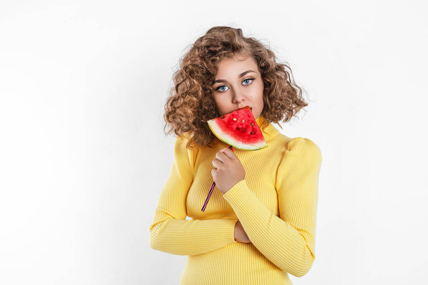 Happy young girl with curly hair holding slice of a watermelon at her face isolated over white background. Afro girl holds watermelon. - Photo, Image