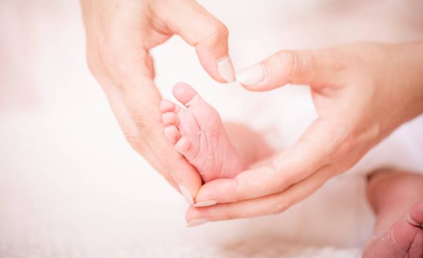 Ноги новорожденного ребенка обнимают мать, формируя сердце. Символизирует любовь, единство, заботу, нежность к ребенку. Новая концепция семьи
. - Фото, изображение