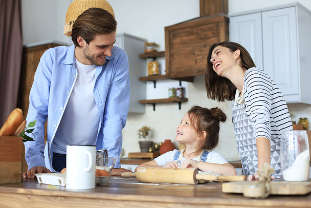 Cute little girl and her parents are having fun while cooking in kitchen at home together - Photo, image