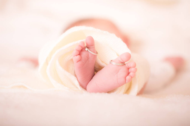 Πόδια νεογέννητου και οι γονείς του βέρες. Τα πόδια ενός νεογέννητου μωρού με τη βέρα της μαμάς σε ένα ζεστό λευκό μάλλινο χαλί. Οικογενειακή ιδέα. Όμορφη εννοιολογική εικόνα της μητρότητας. Κλείσιμο εικόνας. - Φωτογραφία, εικόνα