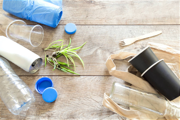 Пластиковий та органічний посуд, посуд, скляна пляшка, еко сумка з молюсків, чашки на дерев'яному тлі з копіювальним простором. екологія, концепція утилізації відходів
. - Фото, зображення
