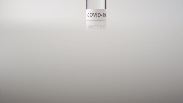 Γυάλινη φύσιγγα με εμβόλιο κορωναϊού σε λευκή επιφάνεια. Πειραματική δόση για βακτηριολογική έρευνα και δοκιμή. Εμβολιασμός από COVID-19 - Πλάνα, βίντεο