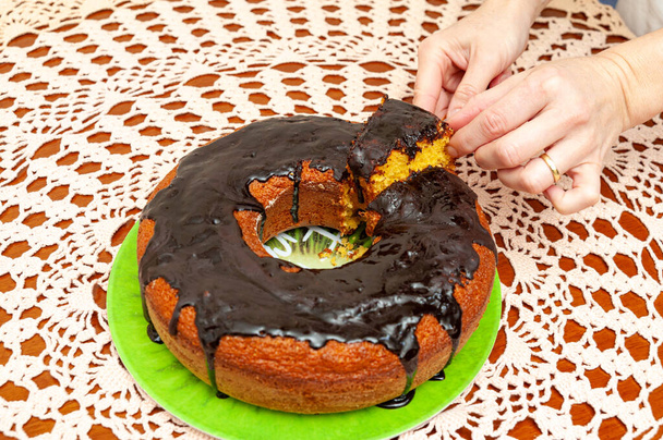 Ręce podnosząc kawałek pyszne i zdrowe tradycyjne brazylijskie domowe ciasto marchewkowe z sosem czekoladowym. Widok góry. Tło ręcznikiem na szydełku. - Zdjęcie, obraz