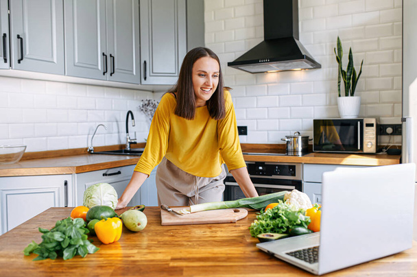 A woman in the kitchen and looks at the laptop  - Photo, image