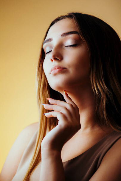 beautiful girl with hands near face on orange colored background, young woman portrait, concept of female beauty - Φωτογραφία, εικόνα