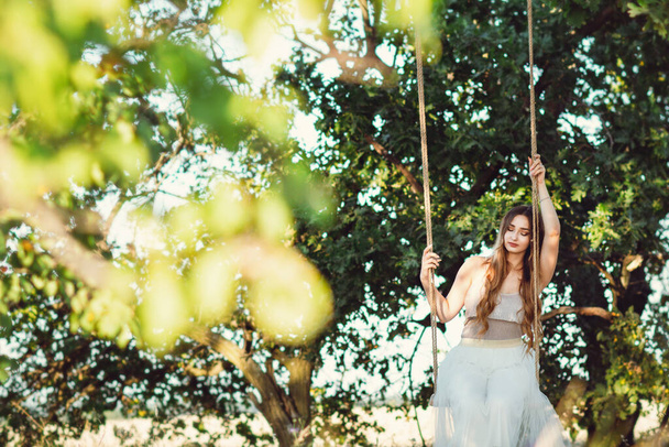 lonely girl with long hair sitting on swing with ropes , young woman enjoy summer nature, leisure activity, lifestyle concept - Φωτογραφία, εικόνα