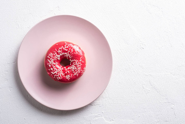 Vaaleanpunainen donitsi sprinkles vaaleanpunainen levy, makea lasitettu jälkiruoka valkoinen betoni kuvioitu tausta, ylhäältä näkymä kopioi tilaa - Valokuva, kuva