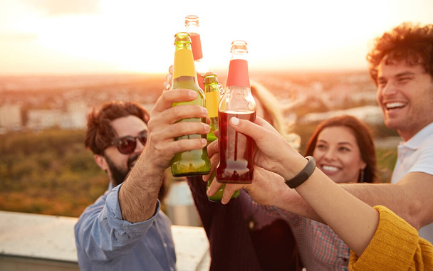 Group of cheerful friends clinking bottles during summer party - Foto, Imagen