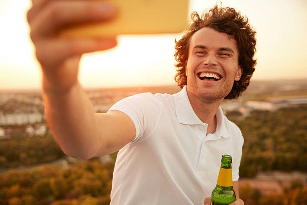 Cheerful guy with beer taking selfie during party - Foto, Bild