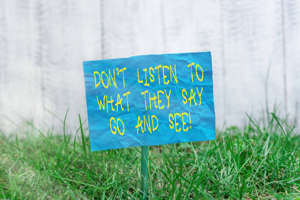 Znak tekstowy: "Nie słuchaj tego, co mówią, idź i zobacz". Koncepcyjne zdjęcie do podróży i zwiedzania świata Zwykły pusty papier przymocowany do patyka i umieszczony w zielonej trawiastej ziemi. - Zdjęcie, obraz