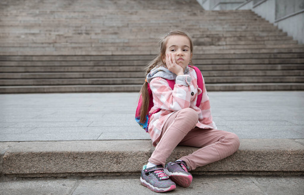 Портрет сумної дівчинки з портретом на спині, що сидить на сходах. Назад до школи
. - Фото, зображення