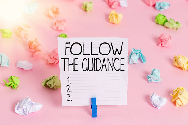 Conceptual hand writing showing Follow The Guidance. Business photo showcasing controlling a course of projectile by builtin mechanism Colored crumpled papers empty reminder pink floor clothespin. - Photo, Image