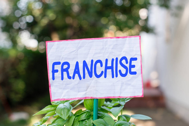 Conceptual hand writing showing Franchise. Business photo showcasing an authorization granted to an individual or group by a government Plain paper attached to stick and placed in the grassy land. - Photo, Image