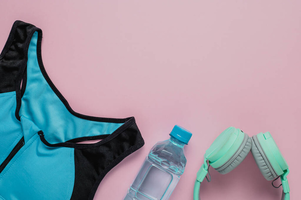 Sutiã esporte para exercício, água potável fresca e fones de ouvido em fundo rosa para esportes e conceito de saúde
 - Foto, Imagem