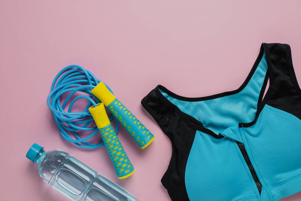 Sport bra for exercise, fresh drinking water and jump rope on pink background for sports and healthcare concept - Photo, Image