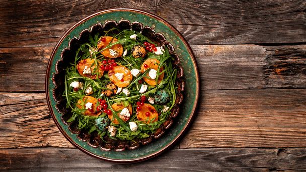 Fresh salad with grilled peach halves, arugula, berries and and goat cheese on a plate on wooden background. Top view. Summer food concept. - Photo, Image