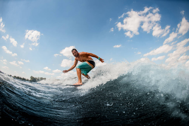 athletic guy wakesurfer actively ride on the waves on surfboard against blue sky - Photo, image