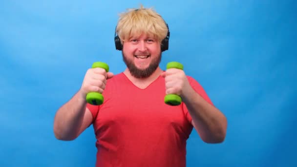 Vicces kövér ember súlyzókkal gyakorolja a kék háttér. - Felvétel, videó