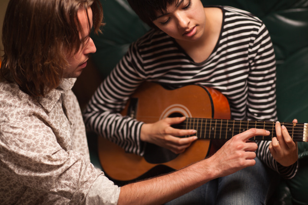 νεαρός μουσικός διδάσκει φοιτήτριας να παίξει την κιθάρα - Φωτογραφία, εικόνα
