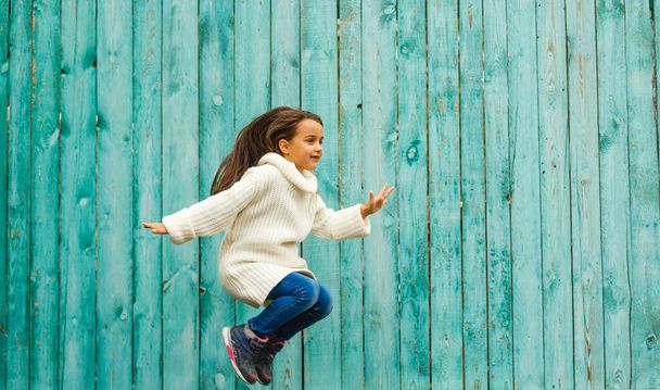 roztomilý holčička v bílém svetru na pozadí modré dřevěné zdi - Fotografie, Obrázek