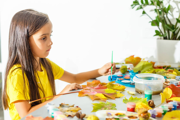 Маленька дівчинка малює на осінньо-жовтому листі з гуашем, дитячим мистецтвом, дитячою творчістю, осіннім мистецтвом
. - Фото, зображення
