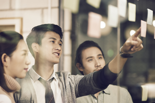 Üç Asyalı küçük şirket işadamı genç girişimciler ofiste tartışırken yapışkan notlar kullanıyorlar. - Fotoğraf, Görsel