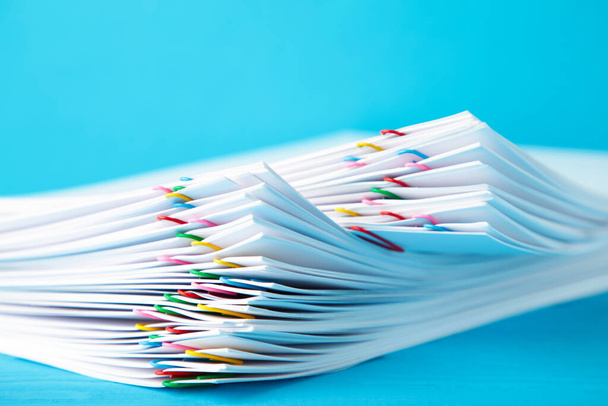 Colorful paper clip with pile of overload white paperwork on blue. Top view - Foto, Bild