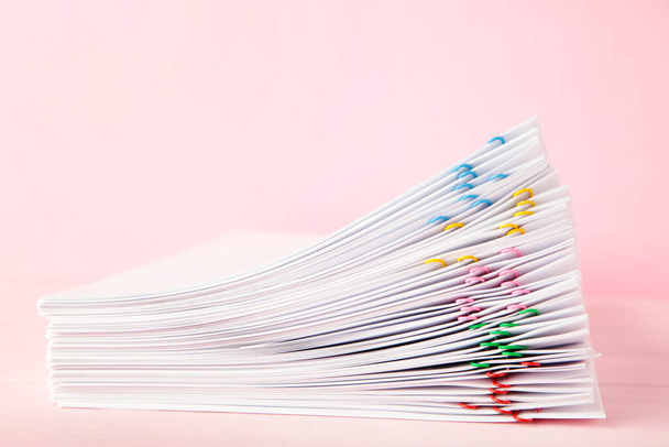 Colorful paper clip with pile of overload white paperwork on pink. Top view - Foto, Bild