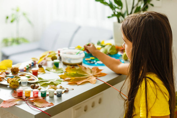 Pintura de niña sobre hojas amarillas otoñales con gouache, artes infantiles, creatividad infantil, arte otoñal. - Foto, imagen