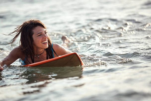 beautiful young caucasian female surfer swimming on surfboard, smiling. copy space - Photo, Image