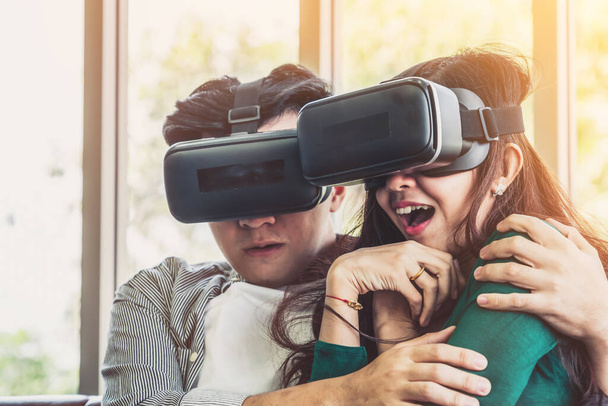 Pareja feliz viendo vídeo en realidad virtual VR auriculares en la sala de estar en casa. Película multimedia y concepto de entretenimiento
. - Foto, Imagen