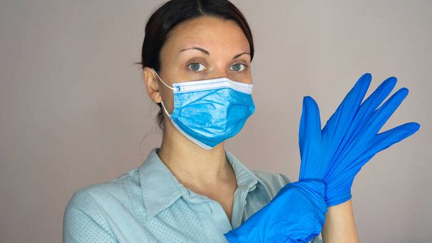 Egy női orvos vagy ápolónő arcmaszkkal kék gumikesztyűt tesz a kezére. - Fotó, kép