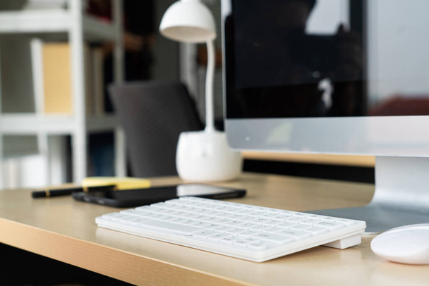 Cierre la computadora de escritorio del teclado en la mesa en una pequeña oficina moderna u oficina en el hogar. Interior del lugar de trabajo de moda. - Foto, Imagen