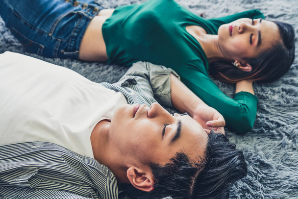 Glückliches asiatisches Paar, das zusammen auf dem Teppich im Wohnzimmer liegt. Liebesbeziehung und Lebensstil-Konzept. - Foto, Bild