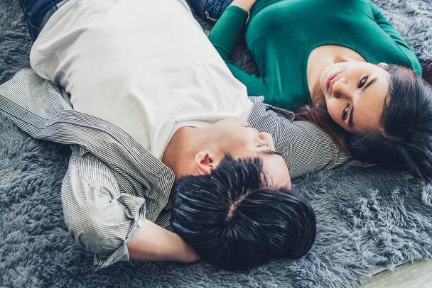 Feliz pareja asiática acostados juntos en la alfombra en el piso de la sala de estar. Amor relación y concepto de estilo de vida
. - Foto, imagen