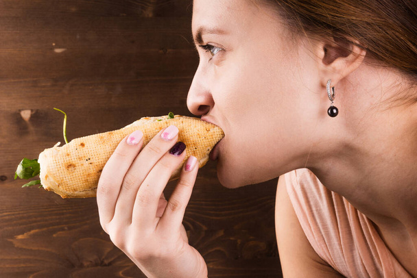 Mujer atractiva joven comiendo perrito caliente en el fondo de la pared de madera marrón, primer plano
 - Foto, imagen