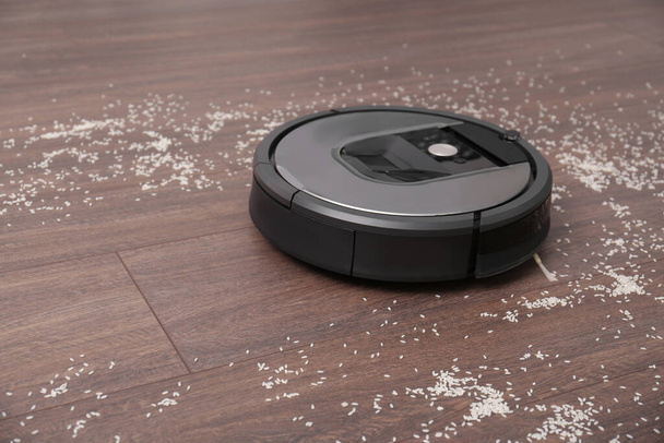 Removing groats from wooden floor with robotic vacuum cleaner at home. Space for text - Foto, Imagen